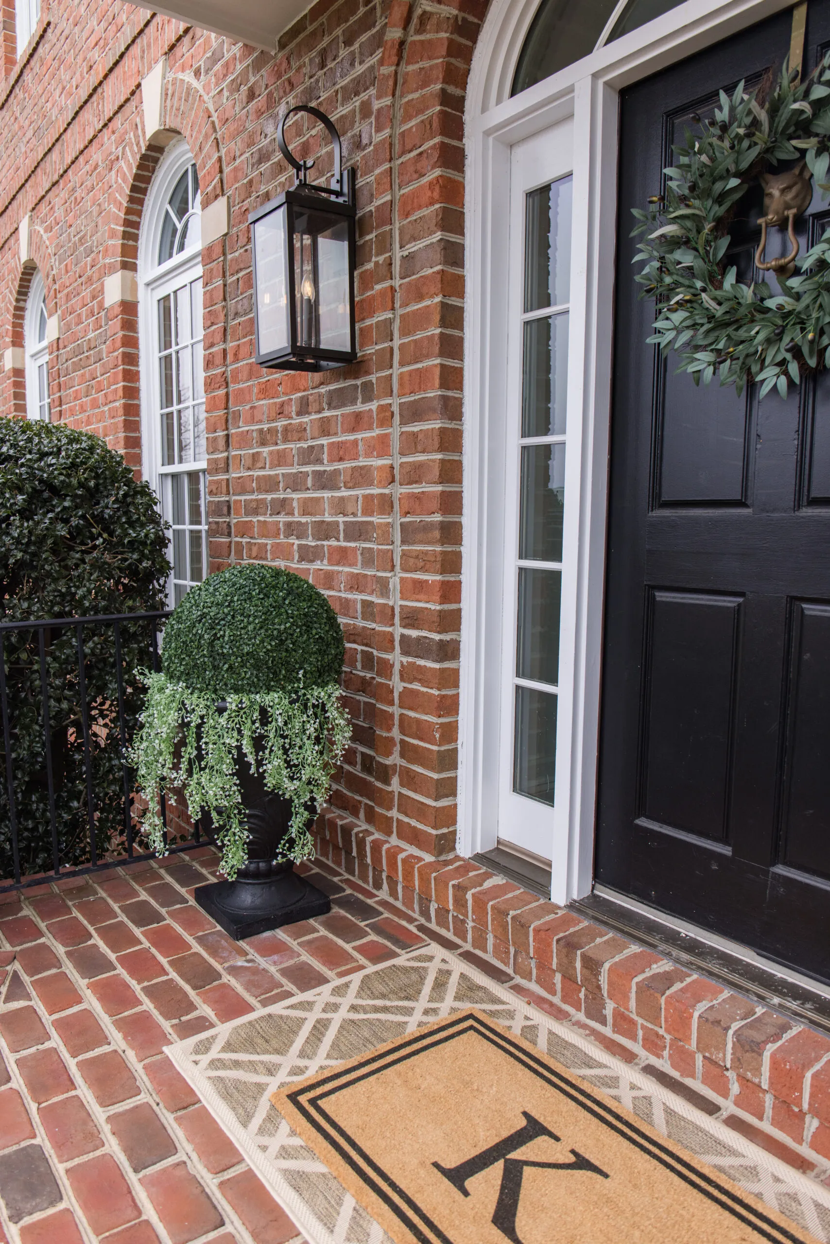 Arched manor spring front porch styling and decor, sconce, faux shrub balls, black planter, hanging plants styled with shrubs, front door wreath