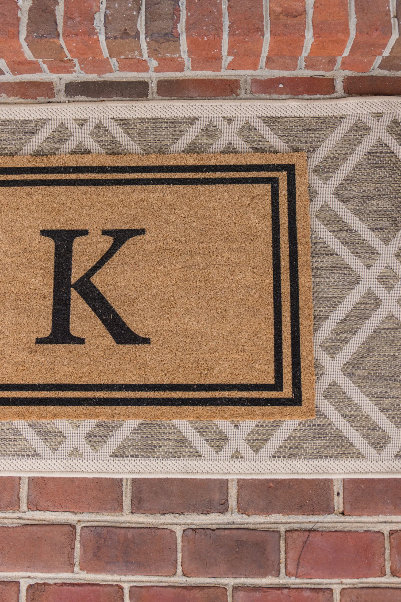 Arched manor spring front porch styling, close-up image of initial doormat layered and styled over a neutral print rug
