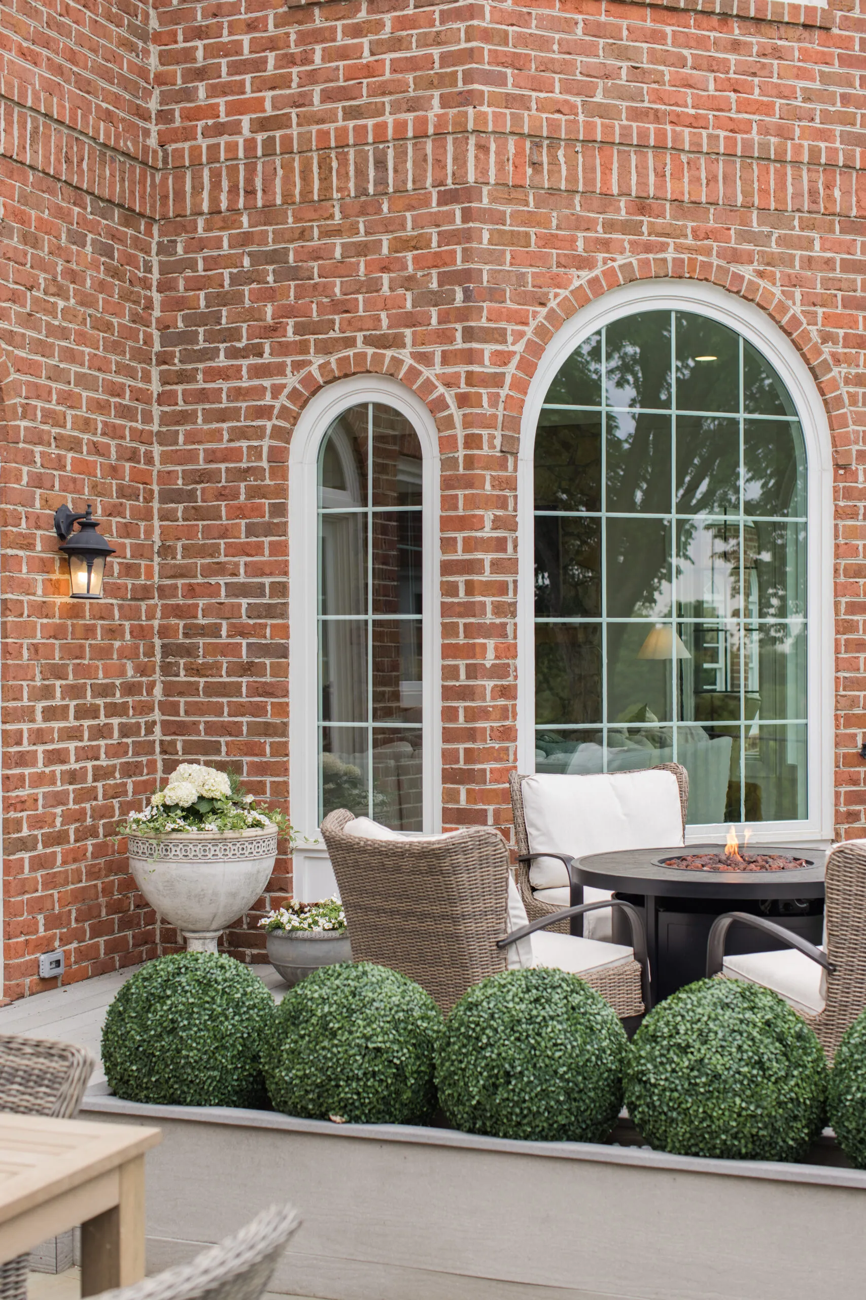 patio styling with wicker chairs surrounding a fire pit table, and four faux shrub balls from Amazon in planter