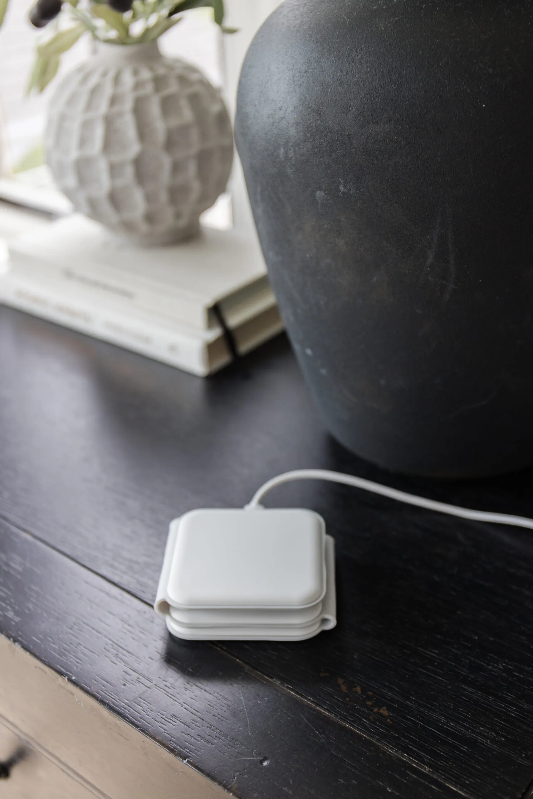Closed 3-in-1 Charging Station next to black lamp on nightstand with white vase filled with faux stems.