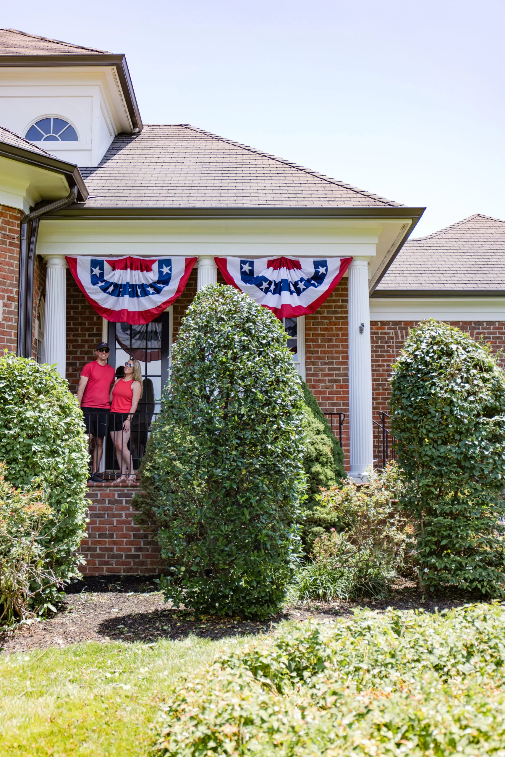 john and megan standing on the arched manor porch with American bunting flags hanging