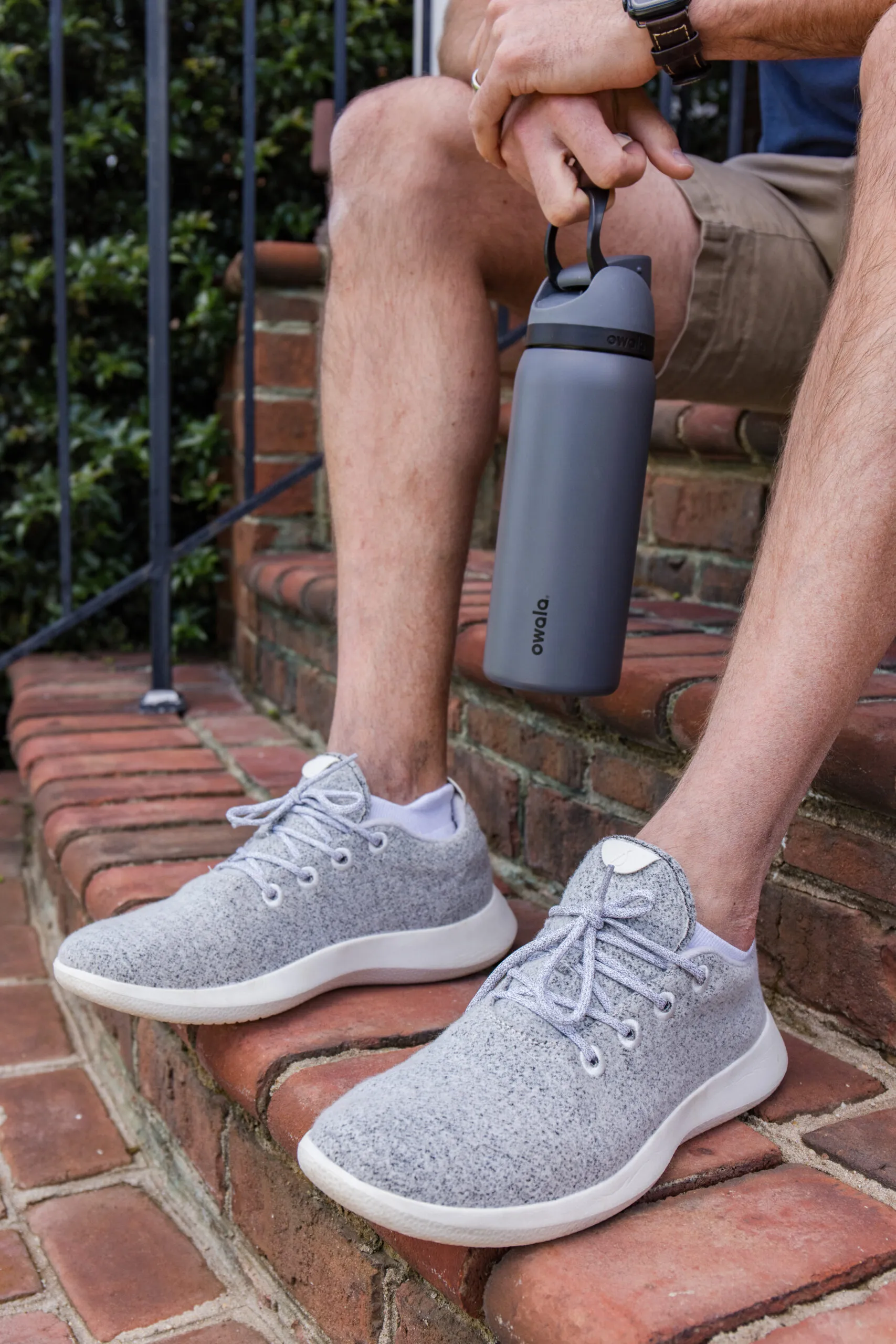 john sitting on front porch steps wearing grey athletic sneakers and holding a water bottle