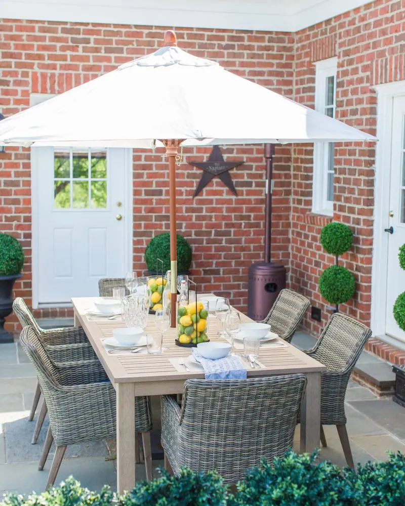 outdoor patio dining table styling with a patio umbrella, wicker patio chairs, artificial lemons and limes decorated in candle lanterns